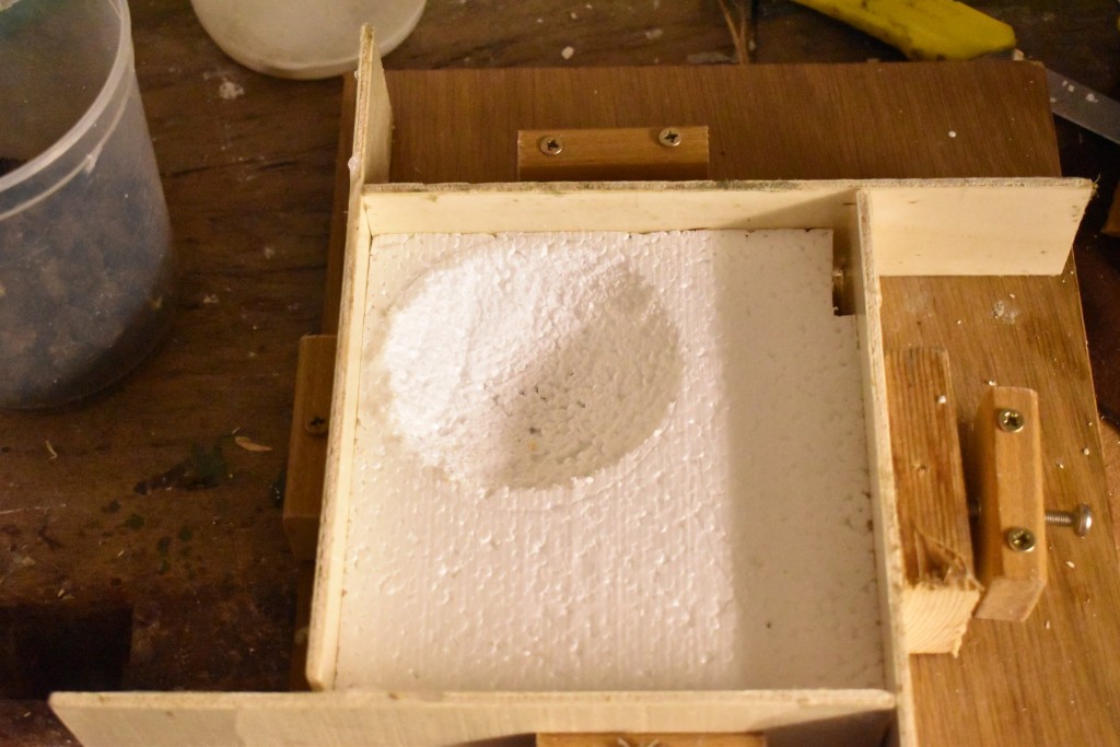 Fertig ausgefräßt. Weil die Muldenplatten in den kleinen Starenkästen sehr genau sein müssen, habe ich sie in eine Vorrichtung gespannt, die verhindern soll, dass später Fliesenkleber außen an der Muldenkonstruktion aushärtet und die Maße verändert. Für normale Nistmulden ist das nicht erforderlich!<br />Rechts oben im Bild die Aussparung für die Halterung der Vorderwand des Starenkastens.